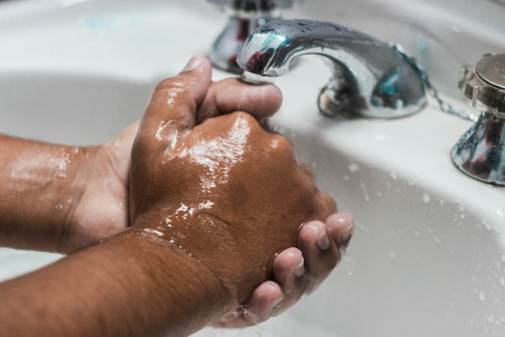 Close-up of two soapy hands being washed under a running faucet at a bathroom sink