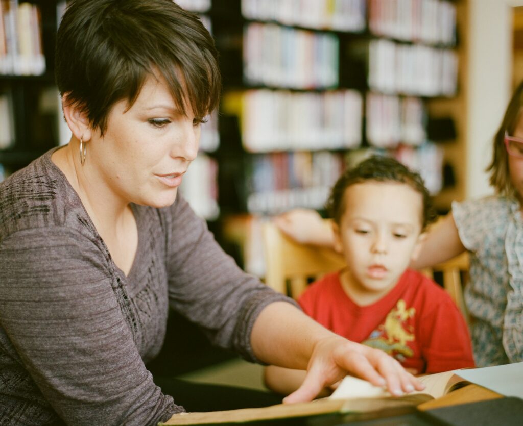 A teacher works at a table with a young boy sitting beside her