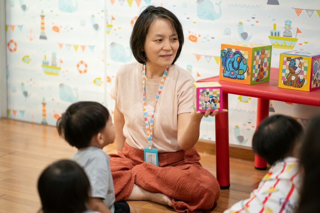 A smiling teacher sits on the floor and shows colorful blocks to a few young children
