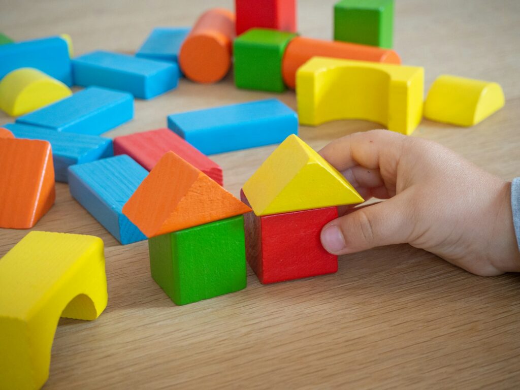 A hand builds a small house from colorful wooden blocks on a table