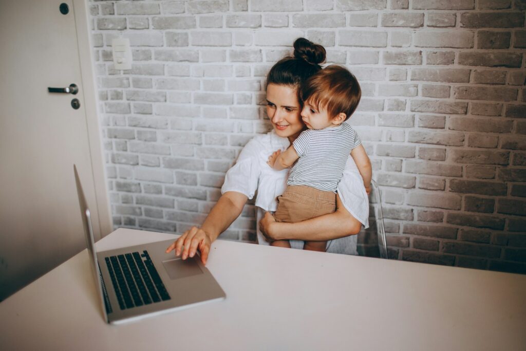 A parent holding a baby at a laptop, illustrating the KidBrief comment policy