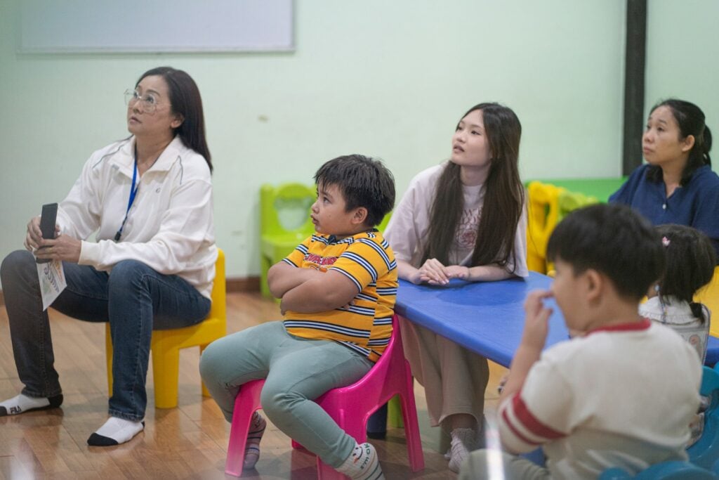 Teachers sit with a small group of young children in a bright classroom