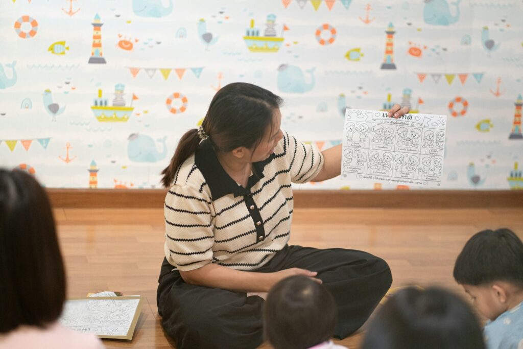 A teacher sits on the floor and holds up a worksheet for a group of young children