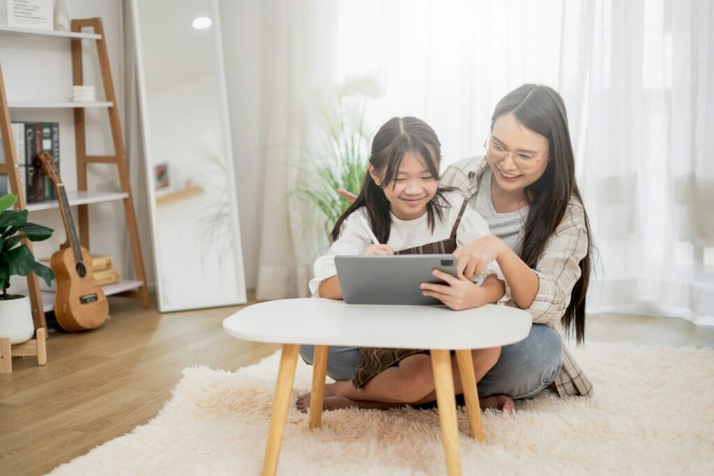 A mother and her daughter sit on the floor looking at a tablet together