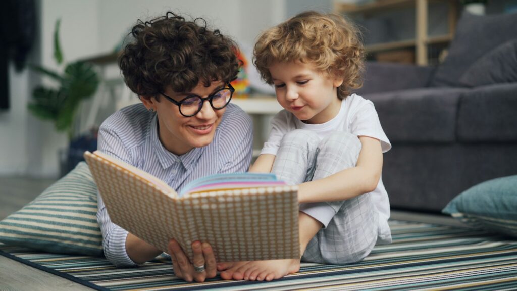A parent and a young child read a picture book together on a striped rug at home