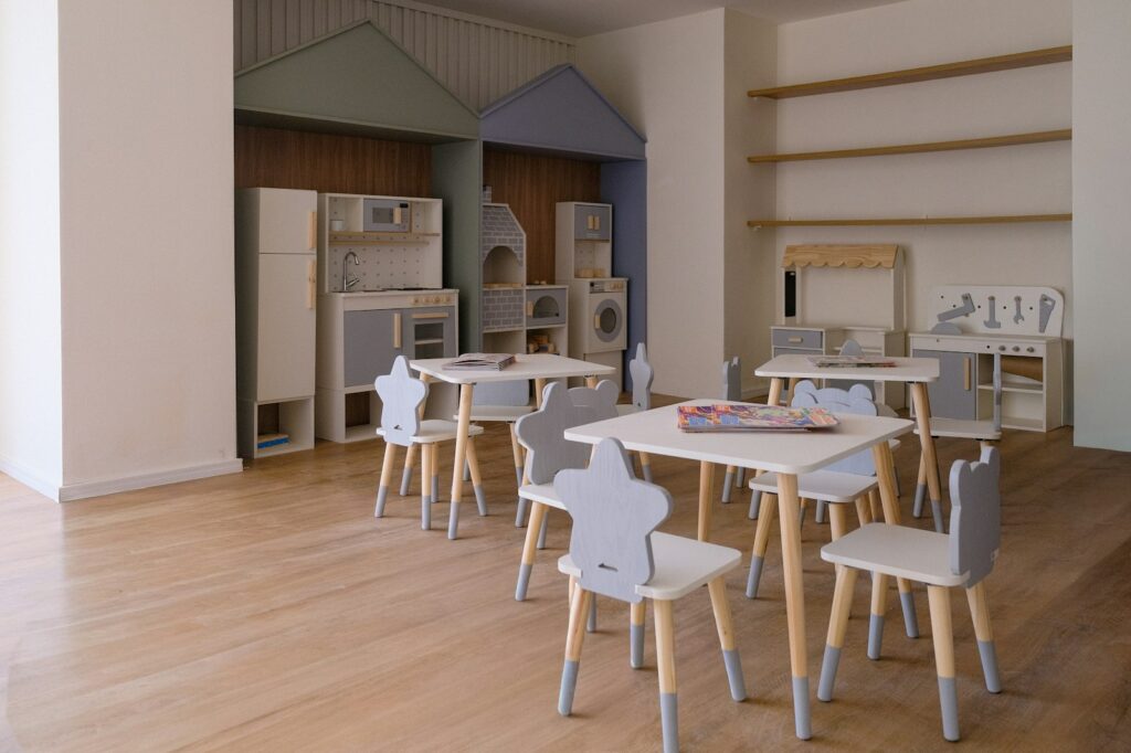 A bright, tidy children's playroom with small tables and chairs and play kitchens